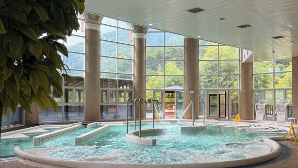 An indoor swimming pool with multiple hot tubs, large windows, and a view of greenery outside. - STX Resort (Mungyeong)
