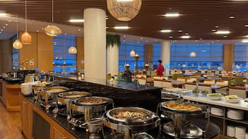 A buffet area with multiple food stations, a seating area with tables and chairs, and a view of the outdoors through large windows.
