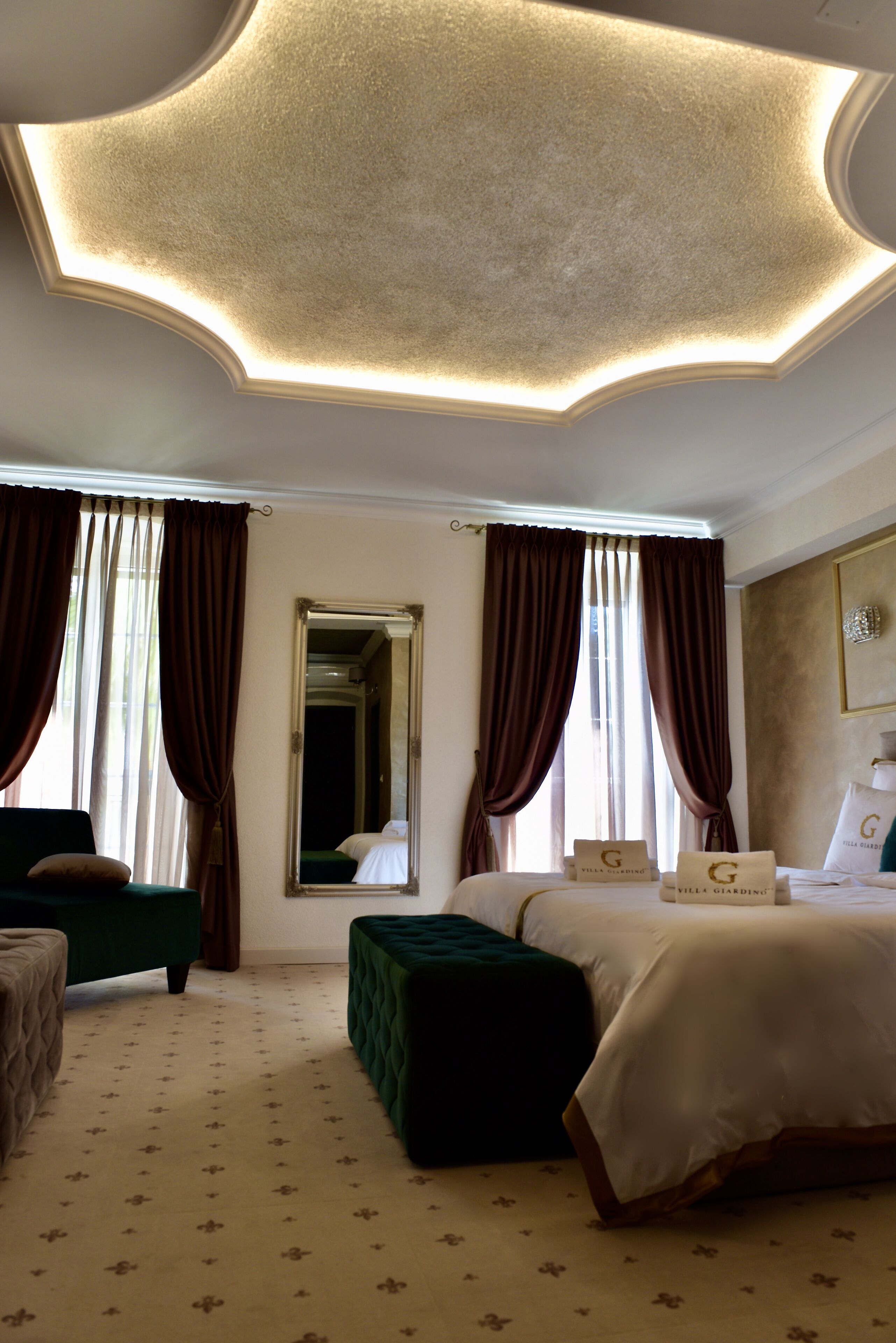 A hotel room with a large bed, a green armchair, a green ottoman, and a mirror on the wall.