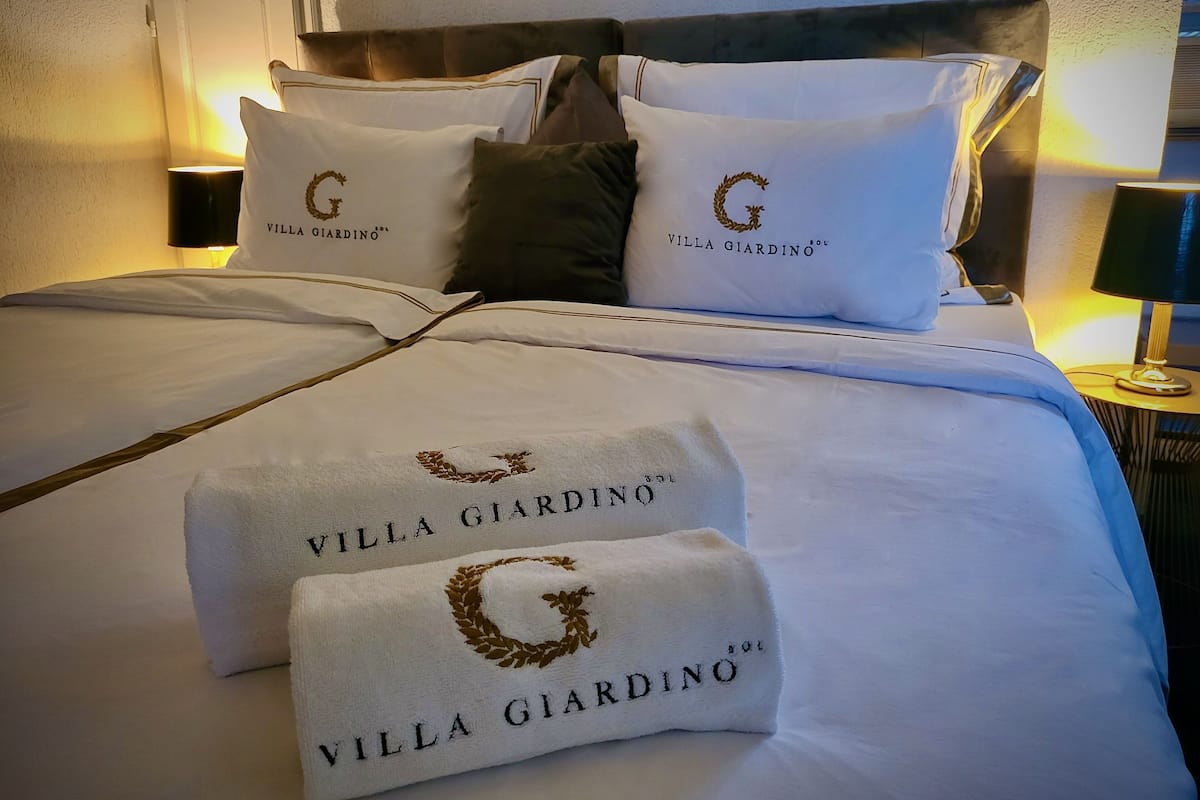 A neatly made bed with white linens and pillows, each featuring the logo "Villa Giardino".