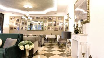 Una habitación con piso a cuadros, un sofá verde, una mesa blanca con una lámpara y una pared decorada con cuadros enmarcados.