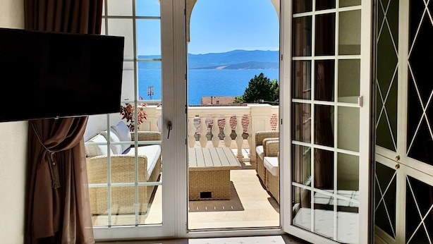 A hotel room with a large bed, a television, and a view of the sea through an open door. - Villa Giardino Heritage Boutique Hotel Bol (Bol)