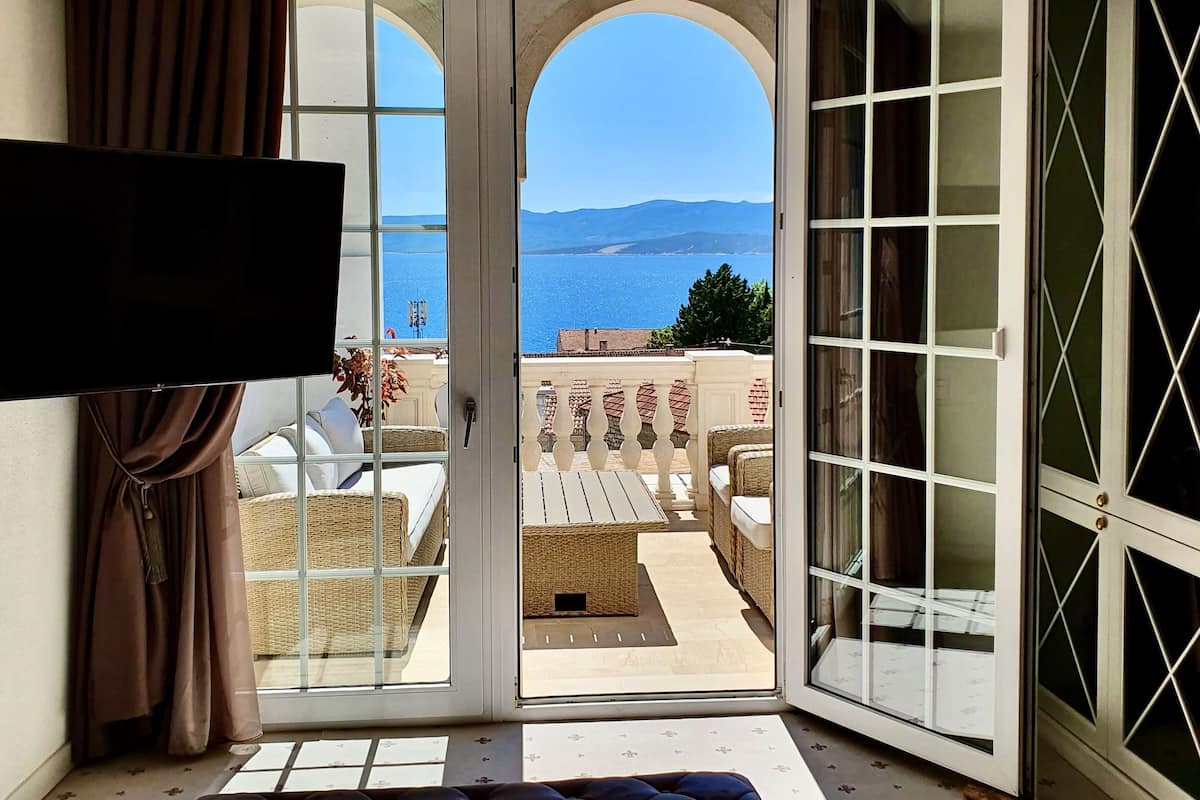 A hotel room with a large bed, a television, and a view of the sea through an open door.