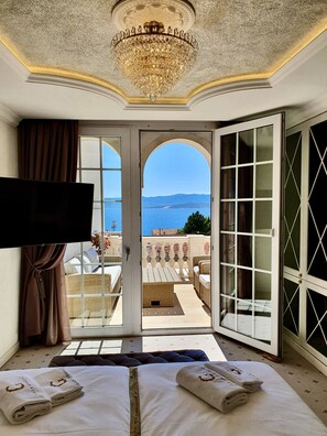 A hotel room with a large bed, a television, and a view of the sea through an open door.
