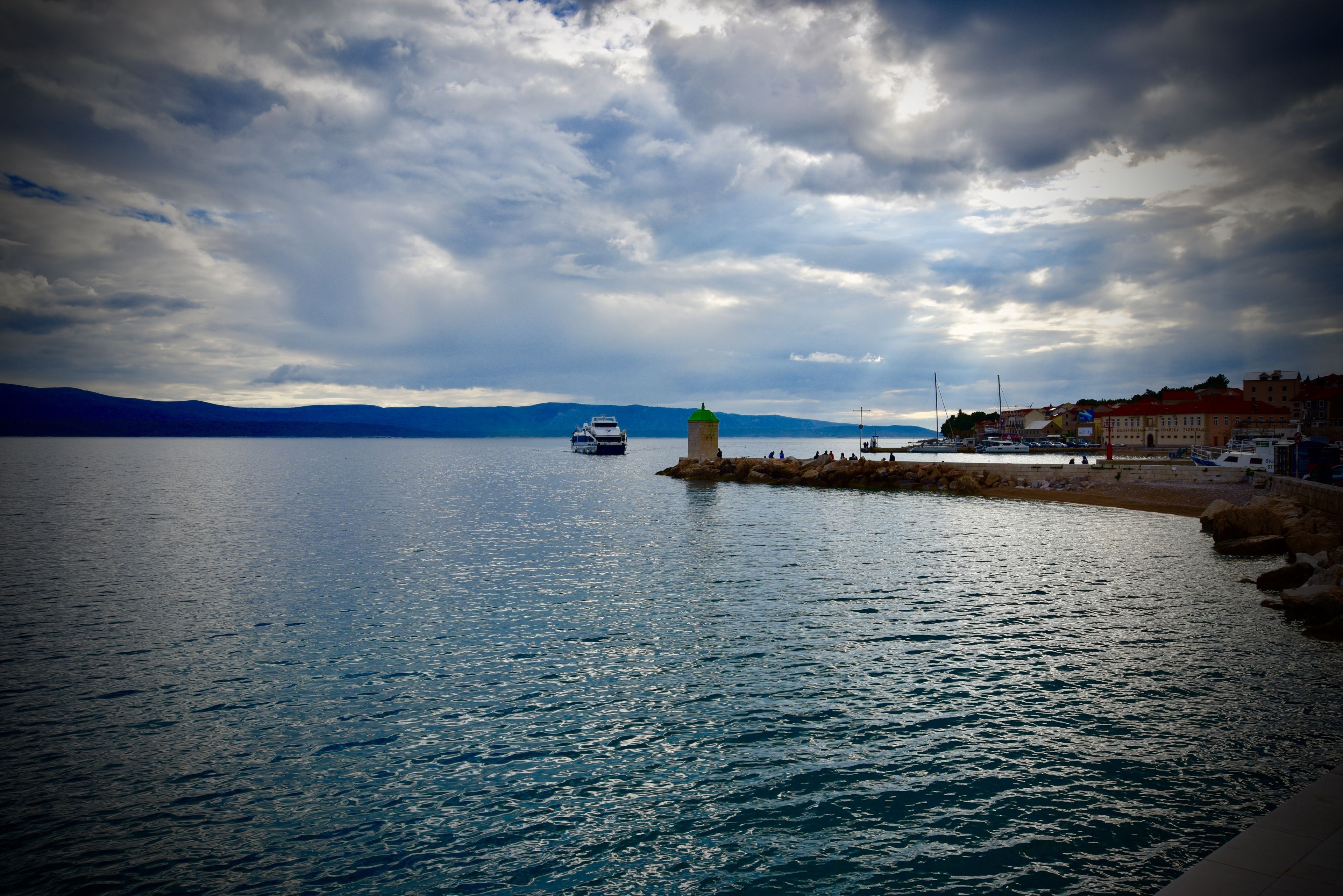 A coastal scene with a lighthouse, calm sea, and distant mountains.
