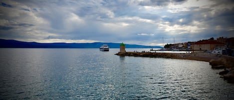 A coastal scene with a lighthouse, calm sea, and distant mountains.