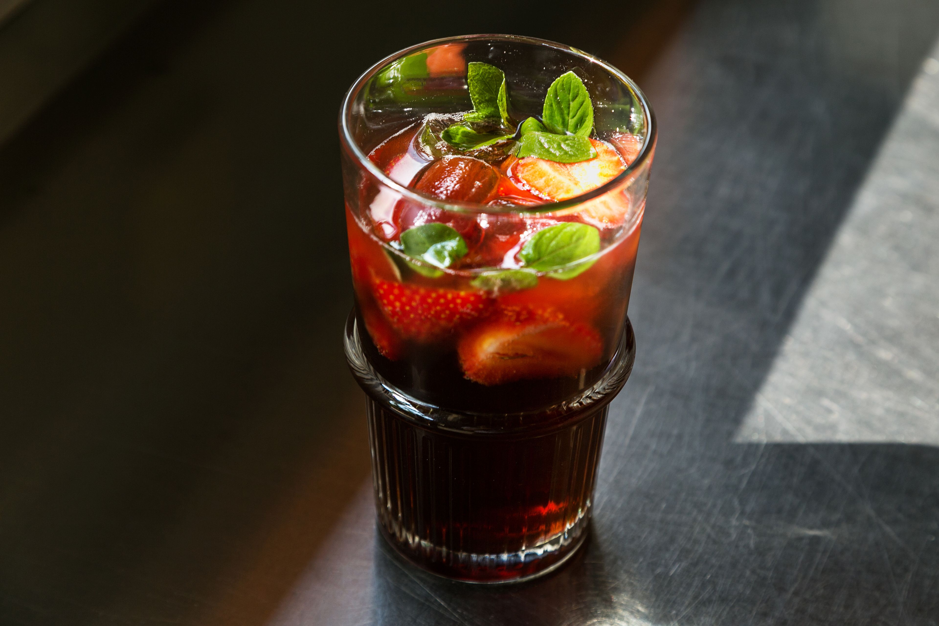 A glass of iced tea with strawberries and mint leaves.