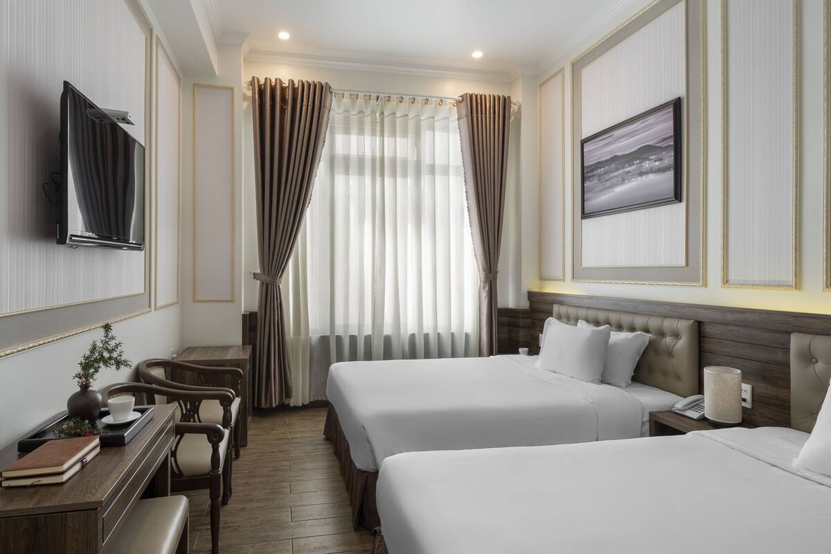 A hotel room with two beds, a TV, a desk with a chair, and a window with curtains.