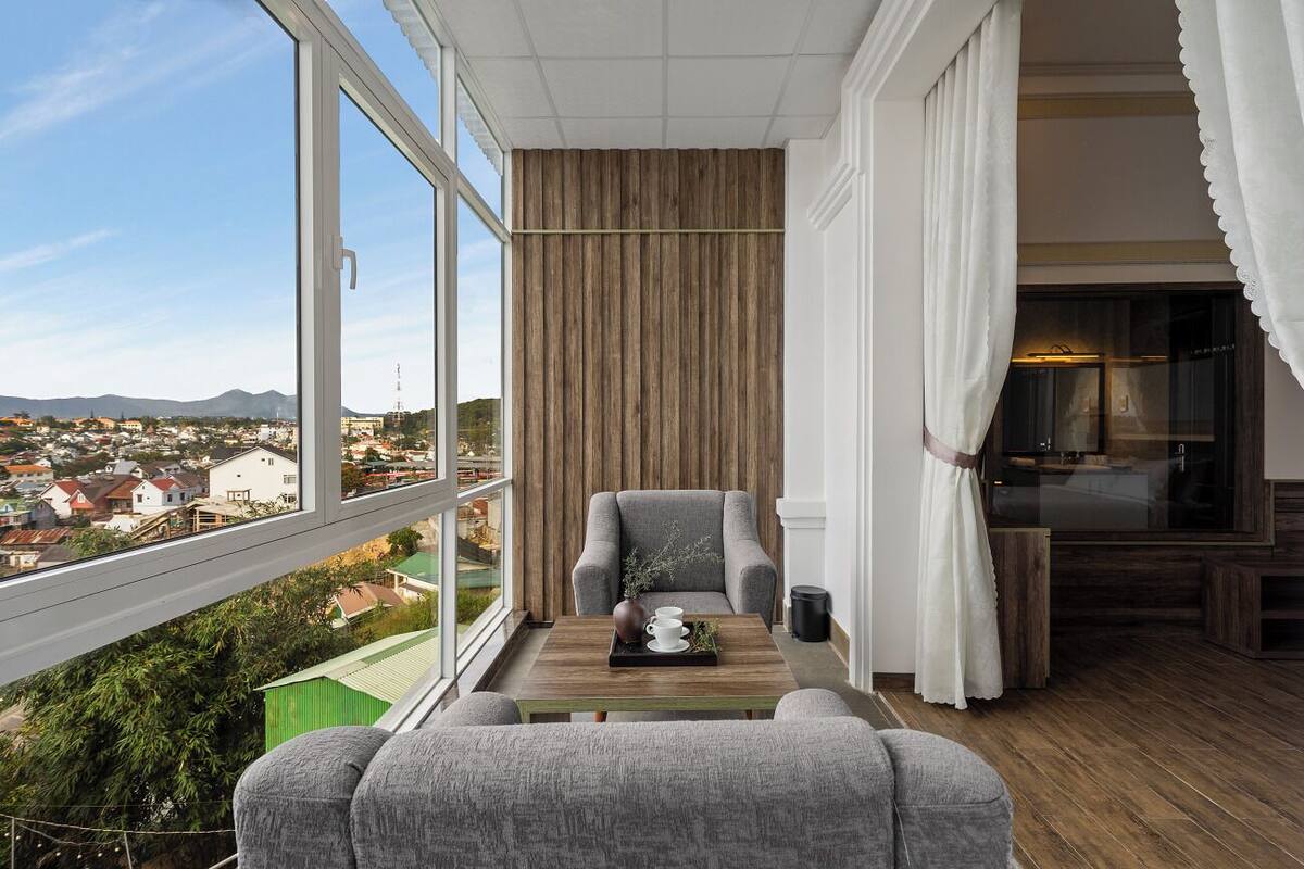 A balcony with a view of a cityscape, a grey armchair, a wooden table with a tray, and a white curtain.