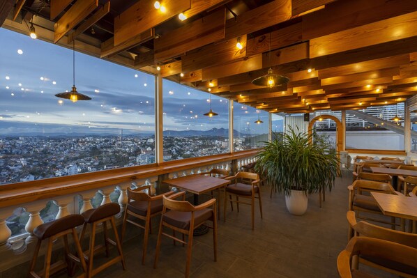 A restaurant with wooden furniture, large windows, and hanging lights.