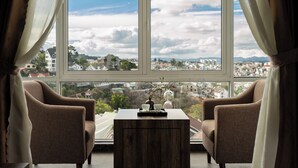 A room with two armchairs and a small table, a large window with curtains, and a view of a cityscape. - New Life Dalat Hotel (Xuan Huong - Da Lat)