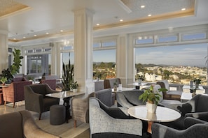 A spacious lounge area with multiple seating options, large windows offering a city view, and a modern ceiling design.