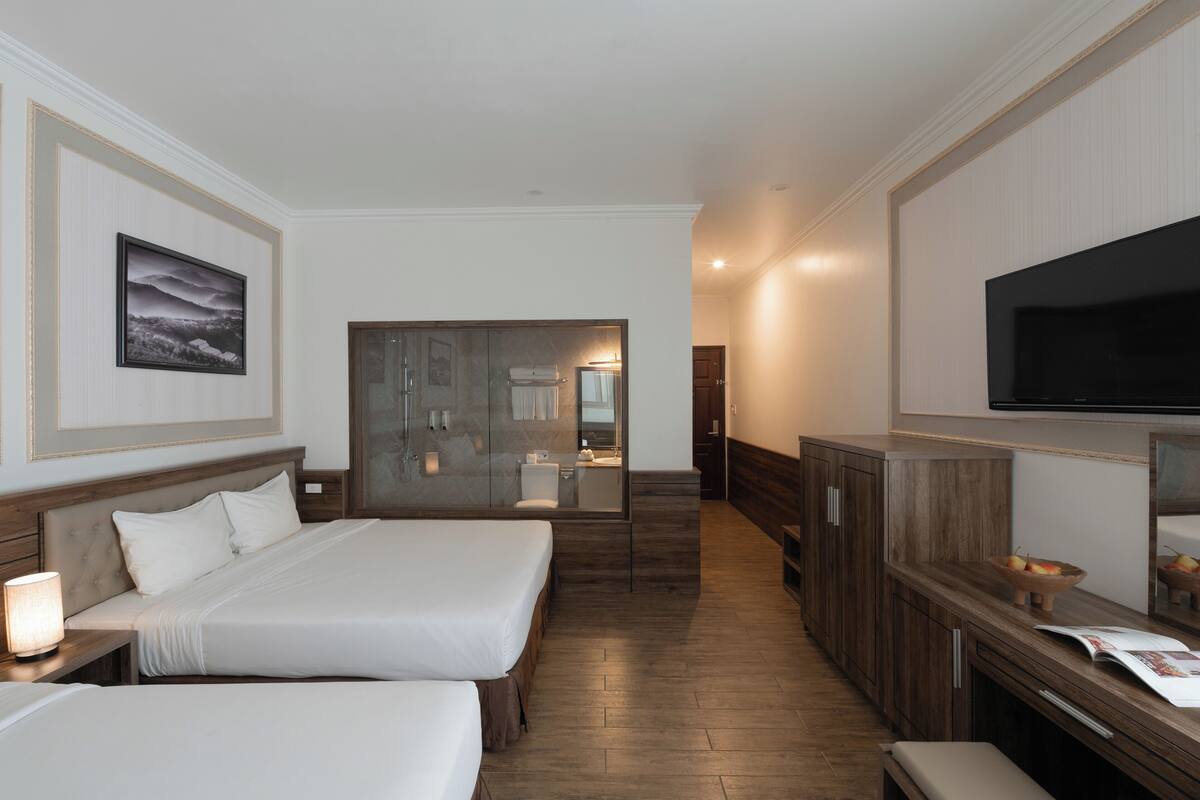 A hotel room with two beds, a TV, a wooden cabinet, and a bathroom visible through a glass door.