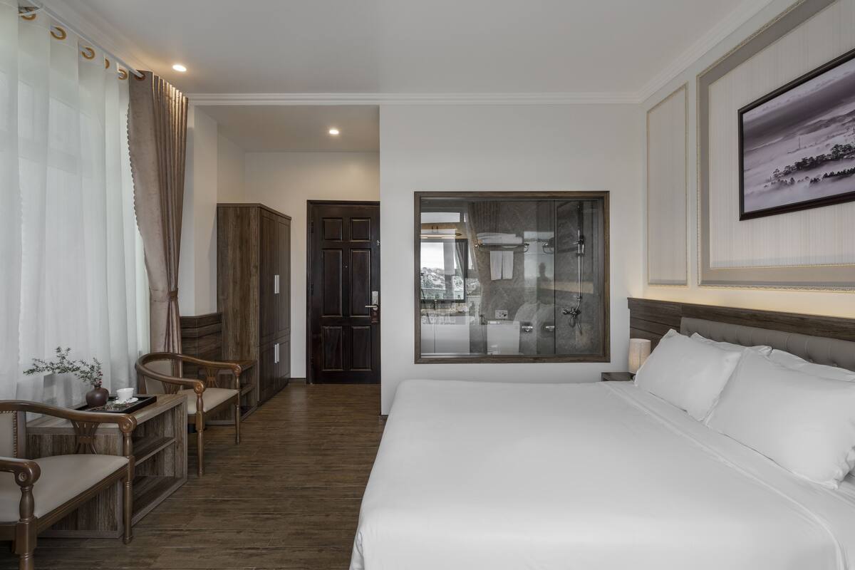 A hotel room with a large bed, wooden furniture, a glass shower enclosure, and a framed picture on the wall.