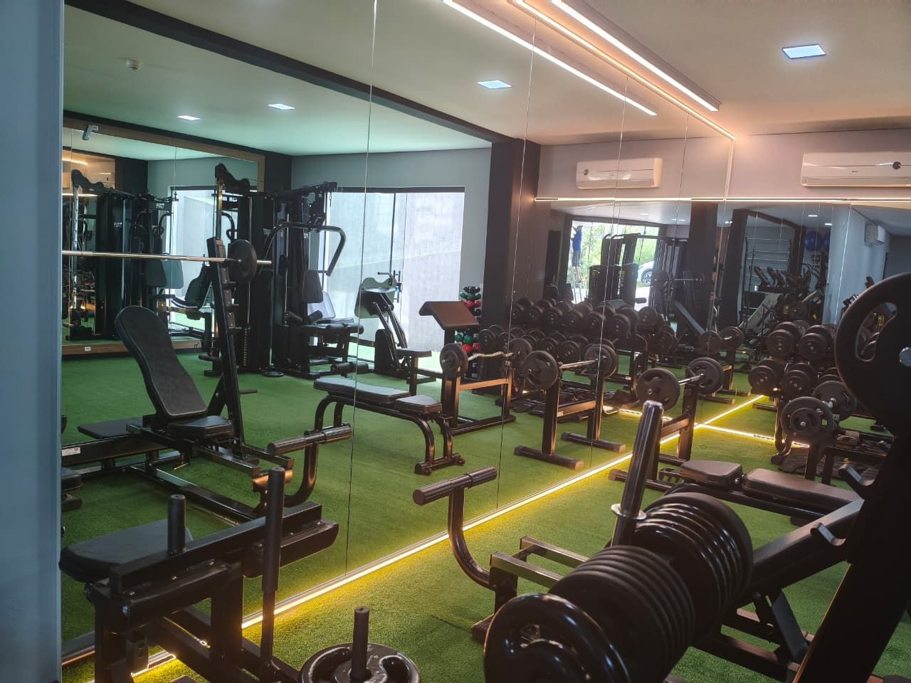 A gym with various exercise equipment, mirrors, and a green carpeted floor.
