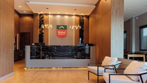 Een hotel receptie met een marmeren balie, een bord met de tekst 'Hotel Bergoglioz' en moderne verlichtingsarmaturen.