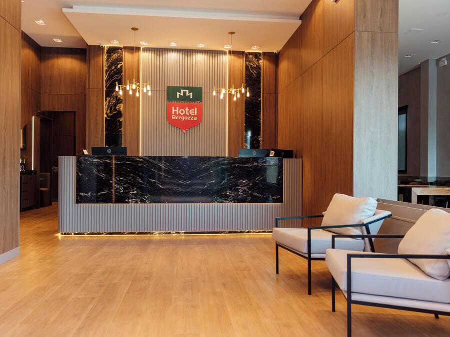 A hotel reception area with a marble reception desk, a sign reading "Hotel Bergoglioz," and modern lighting fixtures.
