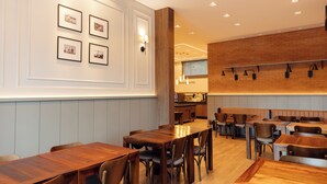 Een restaurant met houten tafels en stoelen, een keukenhoek en wanddecoratie met foto’s.