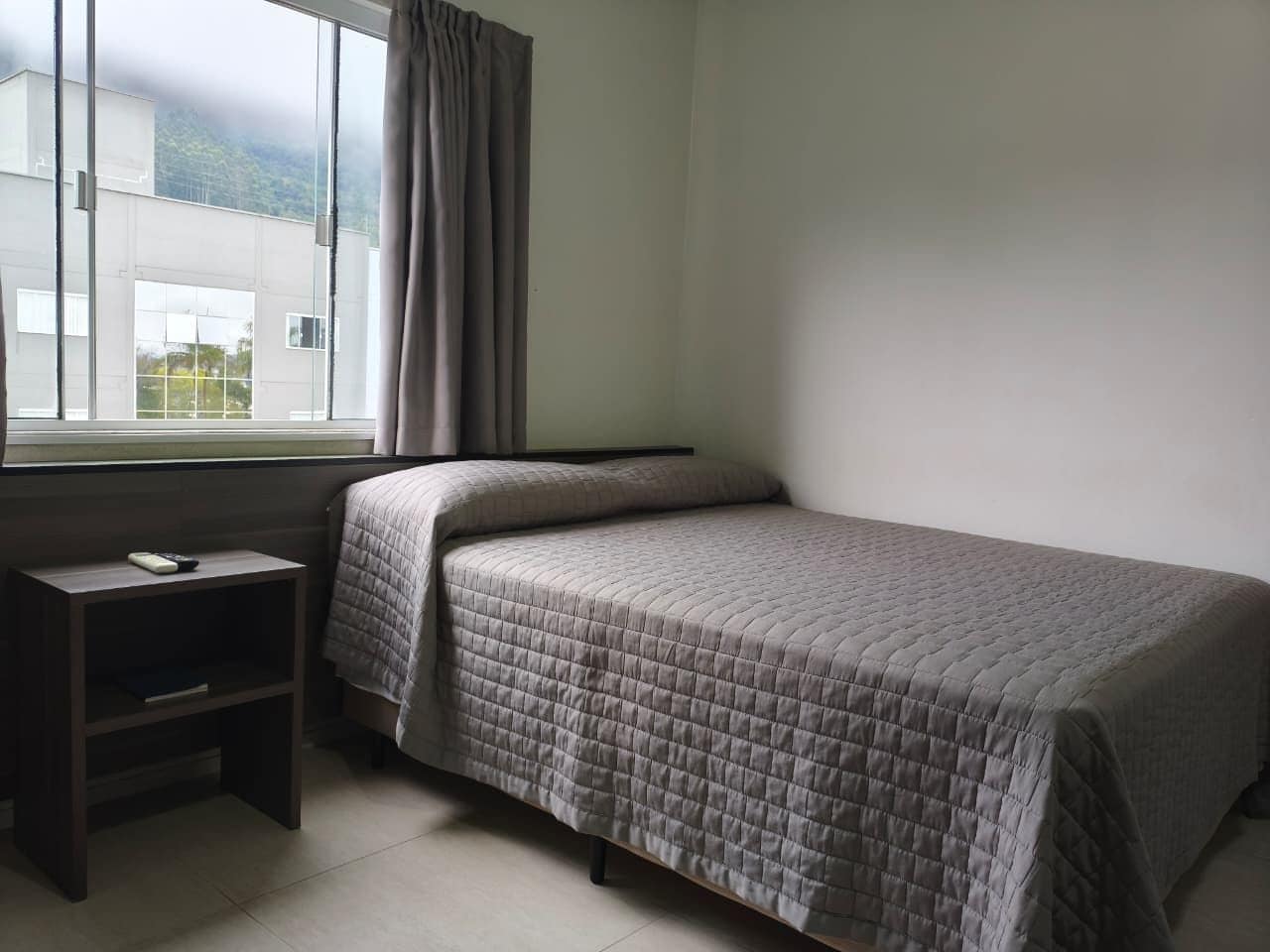 Un dormitorio con una cama, una mesita de noche y una ventana con cortinas.