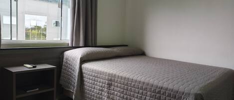 Un dormitorio con una cama, una mesita de noche y una ventana con cortinas.