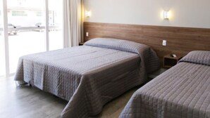 Een hotelkamer met twee bedden, een houten hoofdbord en een groot raam met gordijnen.