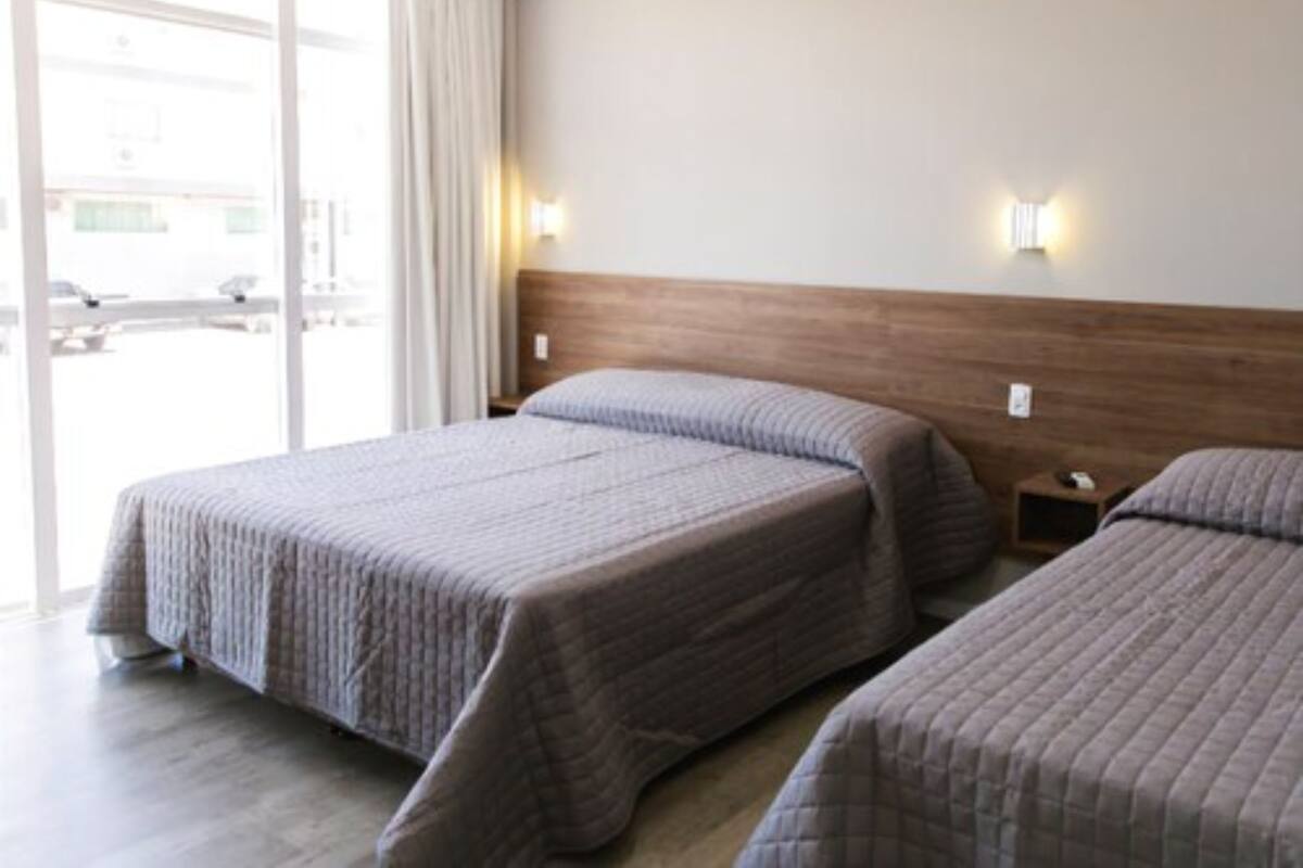 Une chambre d’hôtel avec deux lits, une tête de lit en bois et une grande fenêtre avec des rideaux.