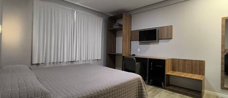 A bedroom with a bed, a desk, a chair, and a television.