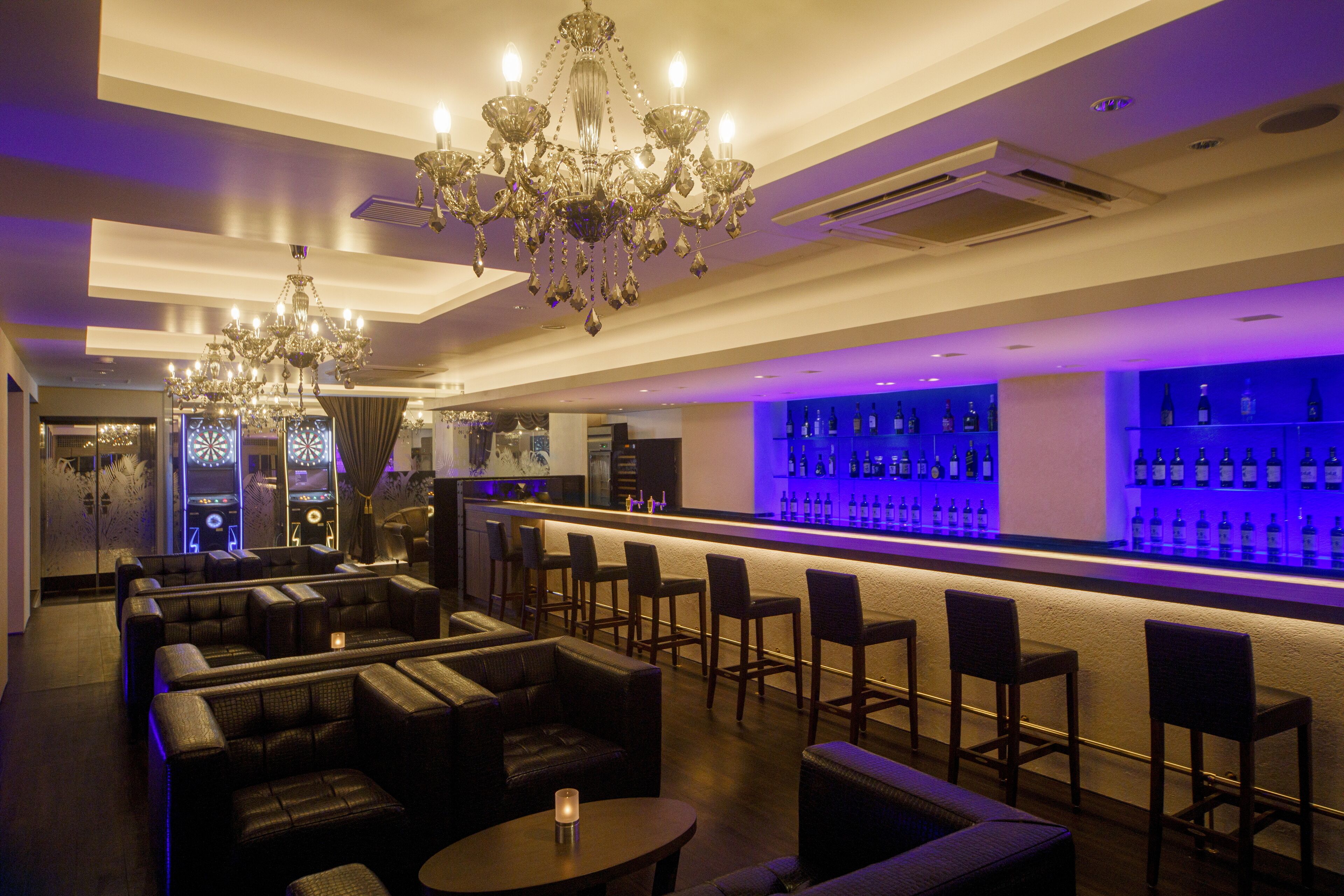 A bar area with leather seating, a chandelier, and a bar stocked with bottles.