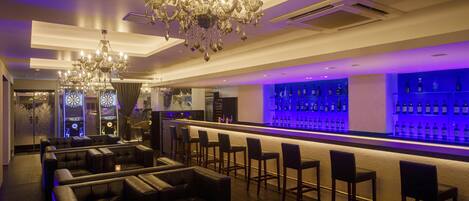 A bar area with leather seating, a chandelier, and a bar stocked with bottles.