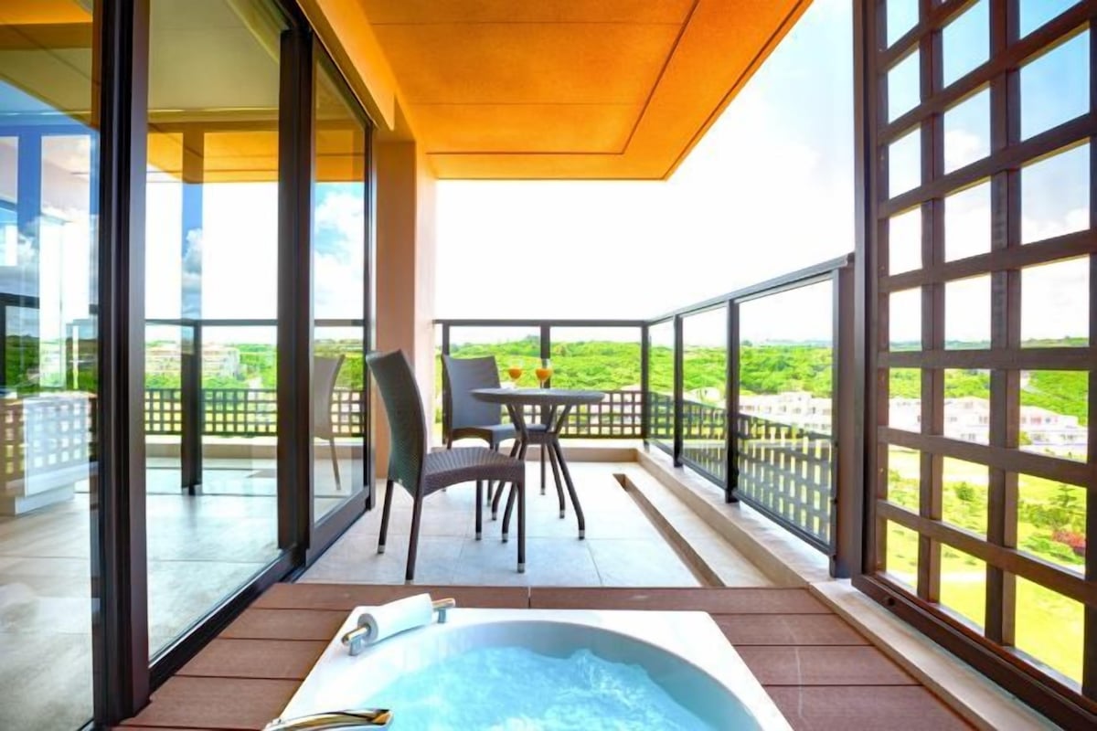 Un balcón con jacuzzi, sillas y una mesa, con vistas a la vegetación.