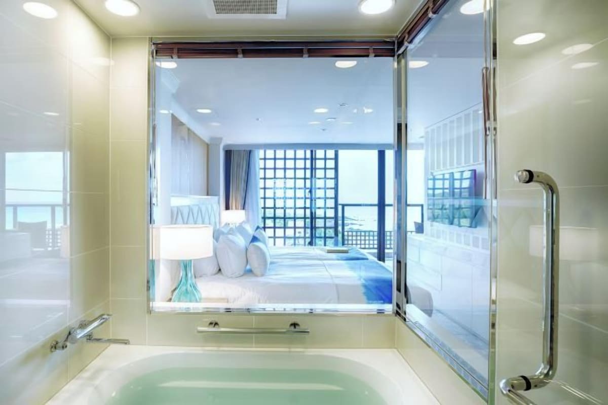 Un baño moderno con ducha de vidrio, una bañera y vistas a un balcón con cama.