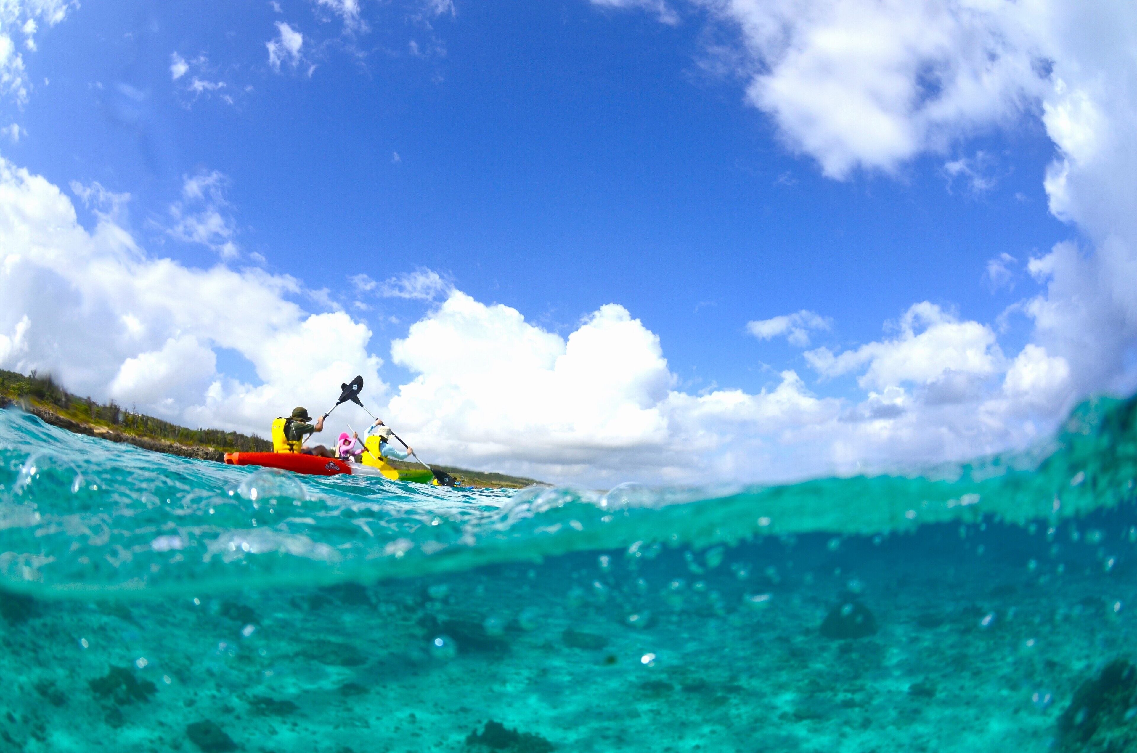 Un kayakista en un kayak rojo sobre un mar turquesa cristalino con un cielo azul brillante y nubes blancas.