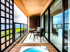 A balcony with a view of the ocean, a hot tub, and a seating area with chairs and a table.