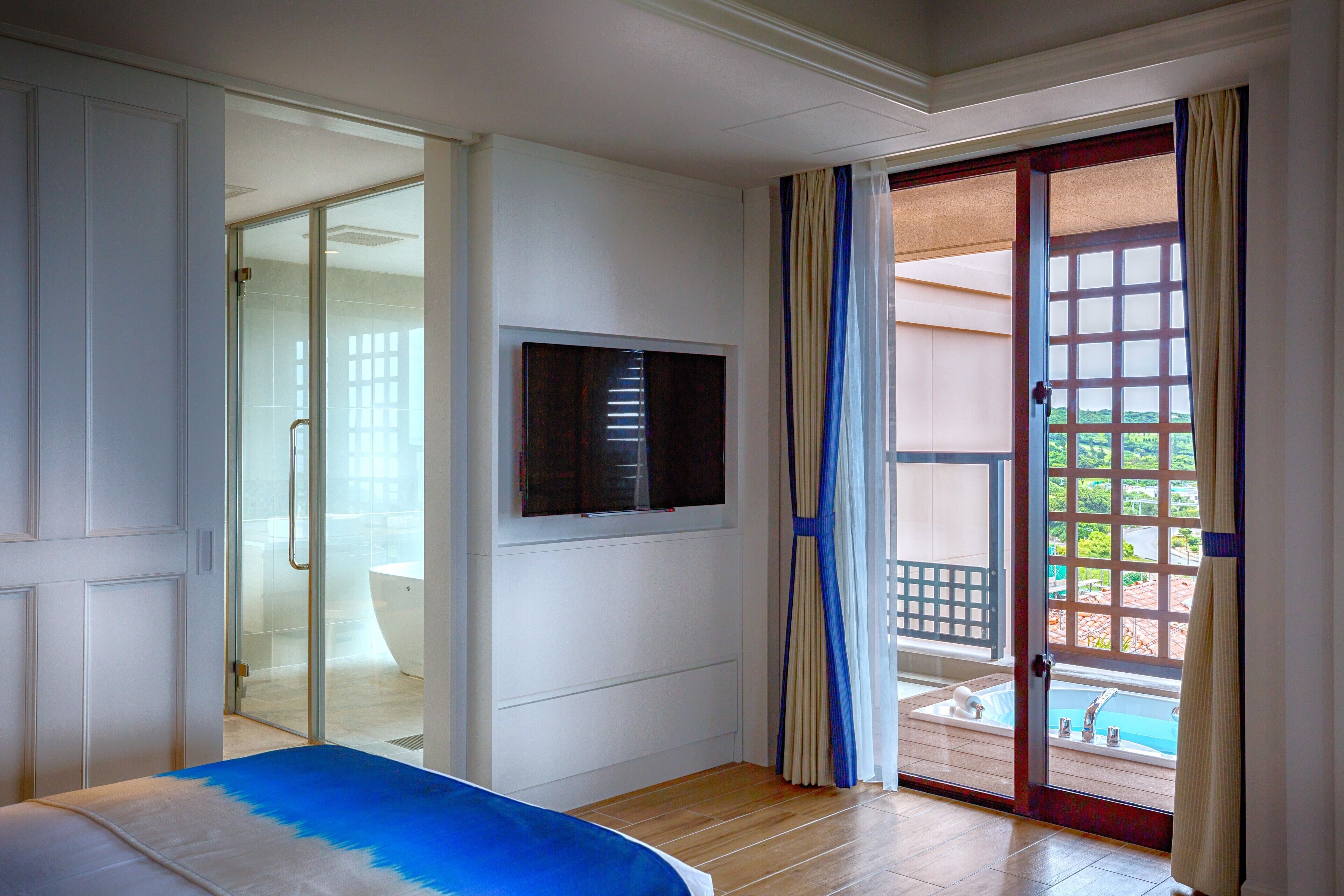 Una camera da letto con un letto, una televisione e una porta vetrata scorrevole che dà su un balcone con piscina.