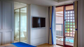 Una camera da letto con un letto, una televisione e una porta vetrata scorrevole che dà su un balcone con piscina.