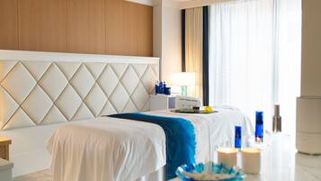 A hotel room with a large bed, a wooden headboard, a bedside table with toiletries, and a window with curtains.