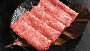 A black plate with pink patterned meat slices and a leaf.