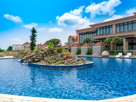 A swimming pool with a rock feature, lounge chairs, and a building with a red roof in the background.