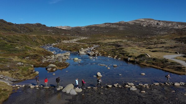 Un arroyo cristalino con rocas, rodeado de colinas cubiertas de hierba y montañas.