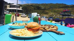 Une table avec un hamburger, des frites et une pizza, avec en arrière-plan une vue sur un immeuble et des voitures.