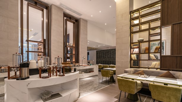 A modern hotel lobby with a marble reception desk, a seating area with yellow chairs, and a bookshelf with framed pictures. - Anban Hotel (Shenzhen)