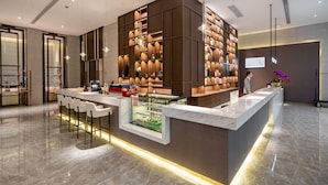 A modern hotel lobby with a marble reception desk, bar seating, and a large wooden shelving unit with books and decorative items. - Anban Hotel (Shenzhen)