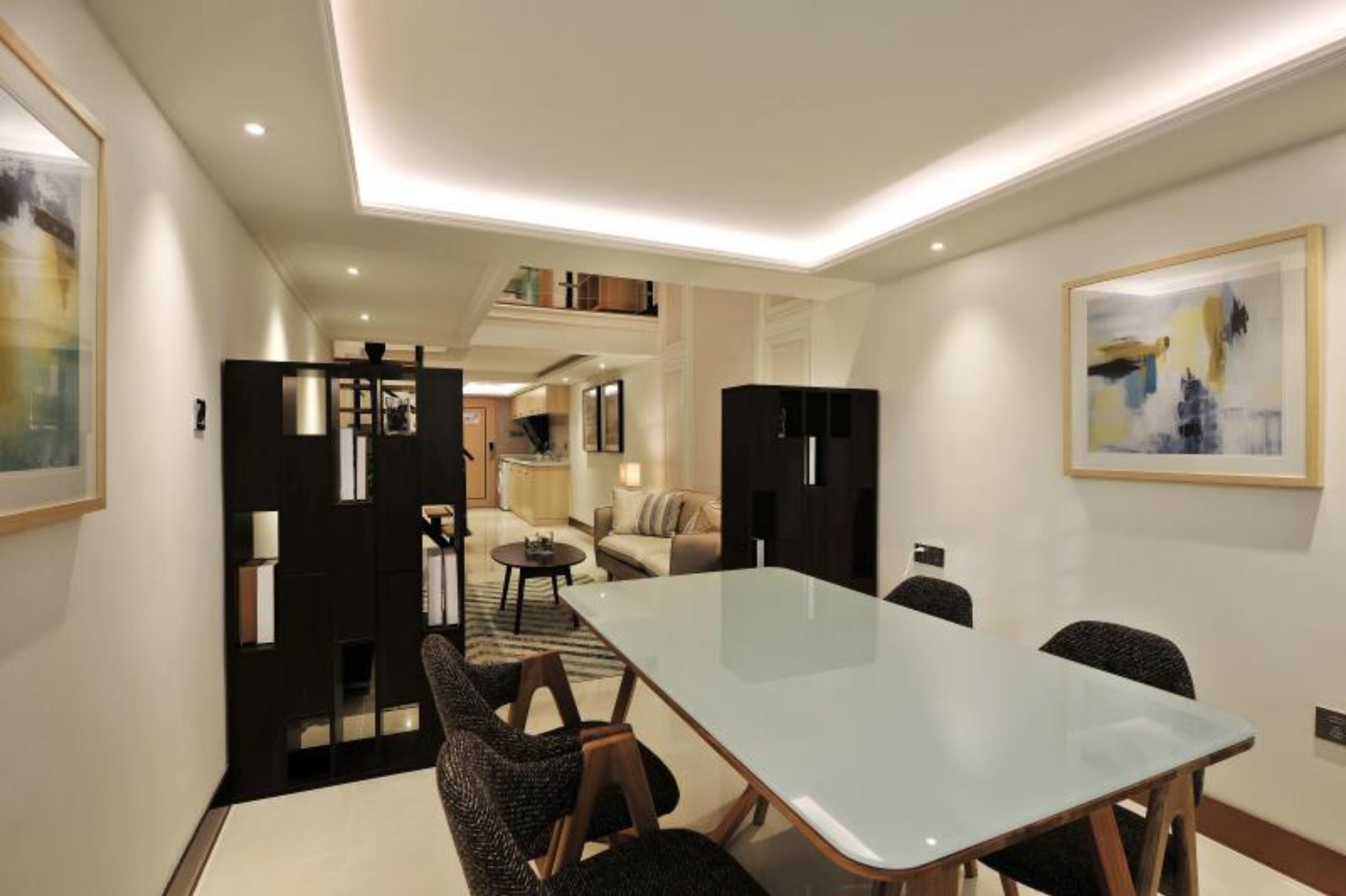 A modern hotel room with a glass dining table, a sofa, a small coffee table, and a bookshelf.