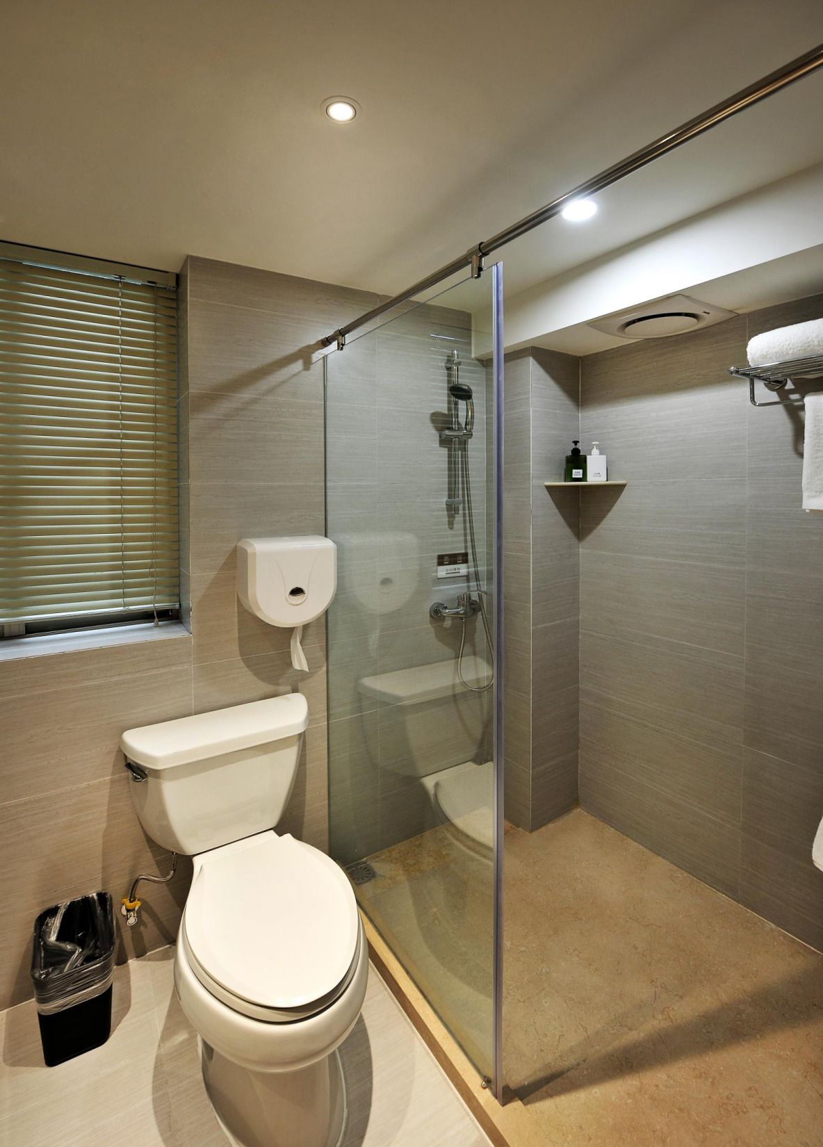 A modern bathroom with a glass-enclosed shower, a toilet, and a hand dryer.