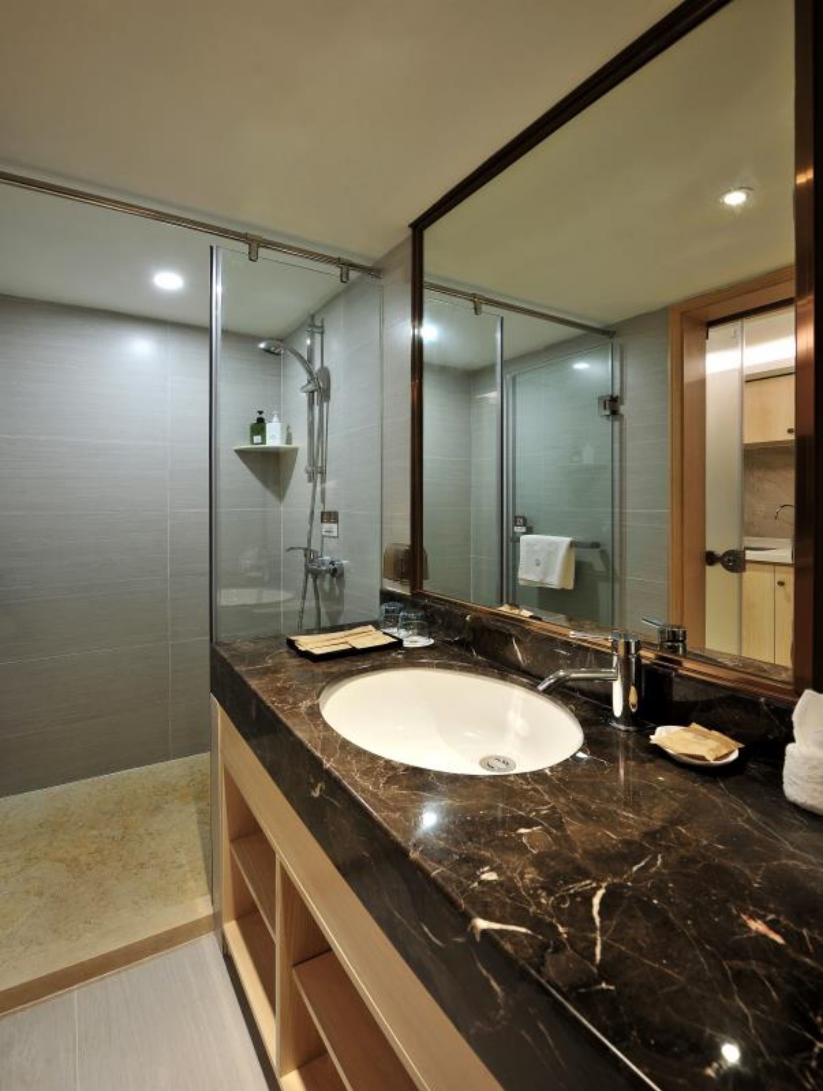 A modern bathroom with a large mirror, a white sink, and a glass-enclosed shower.