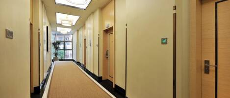 A hotel hallway with carpeted floors, wooden doors, and ceiling lights.