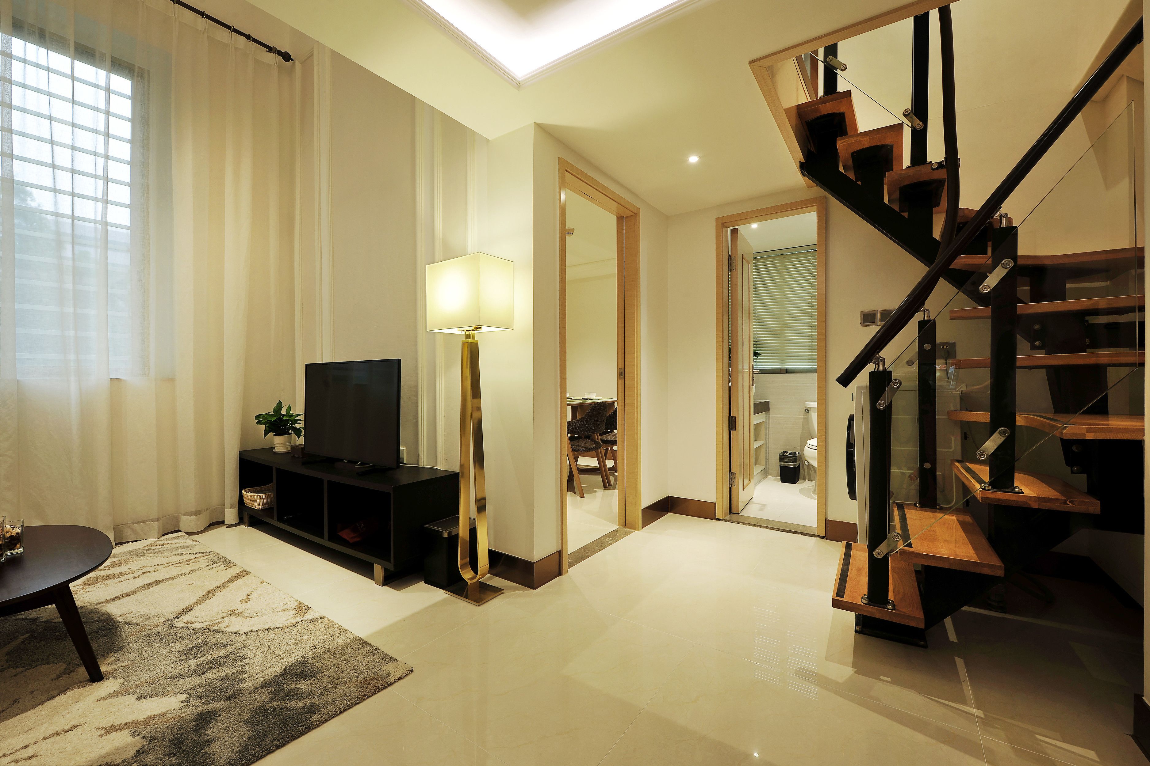 A modern living room with a flat-screen TV, a lamp, a sofa, and a staircase.