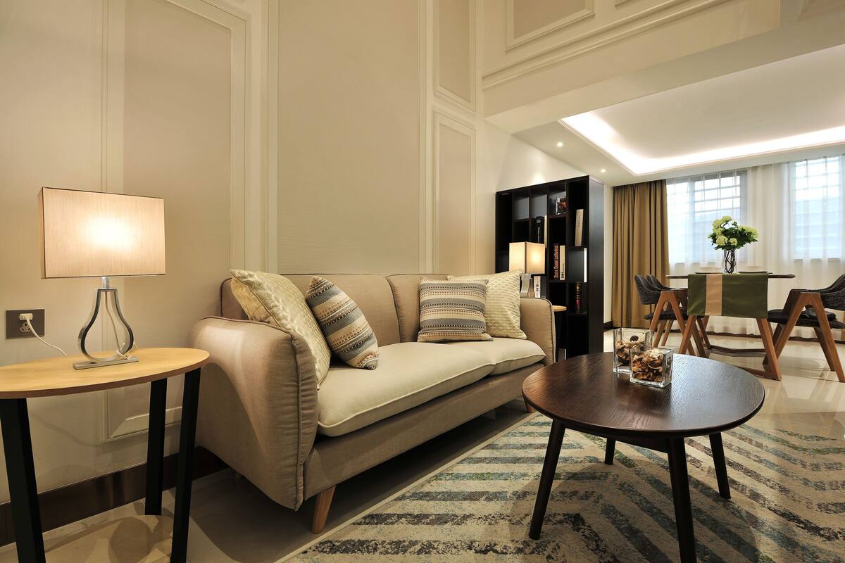A modern living room with a sofa, a round coffee table, a side table, and a bookshelf.