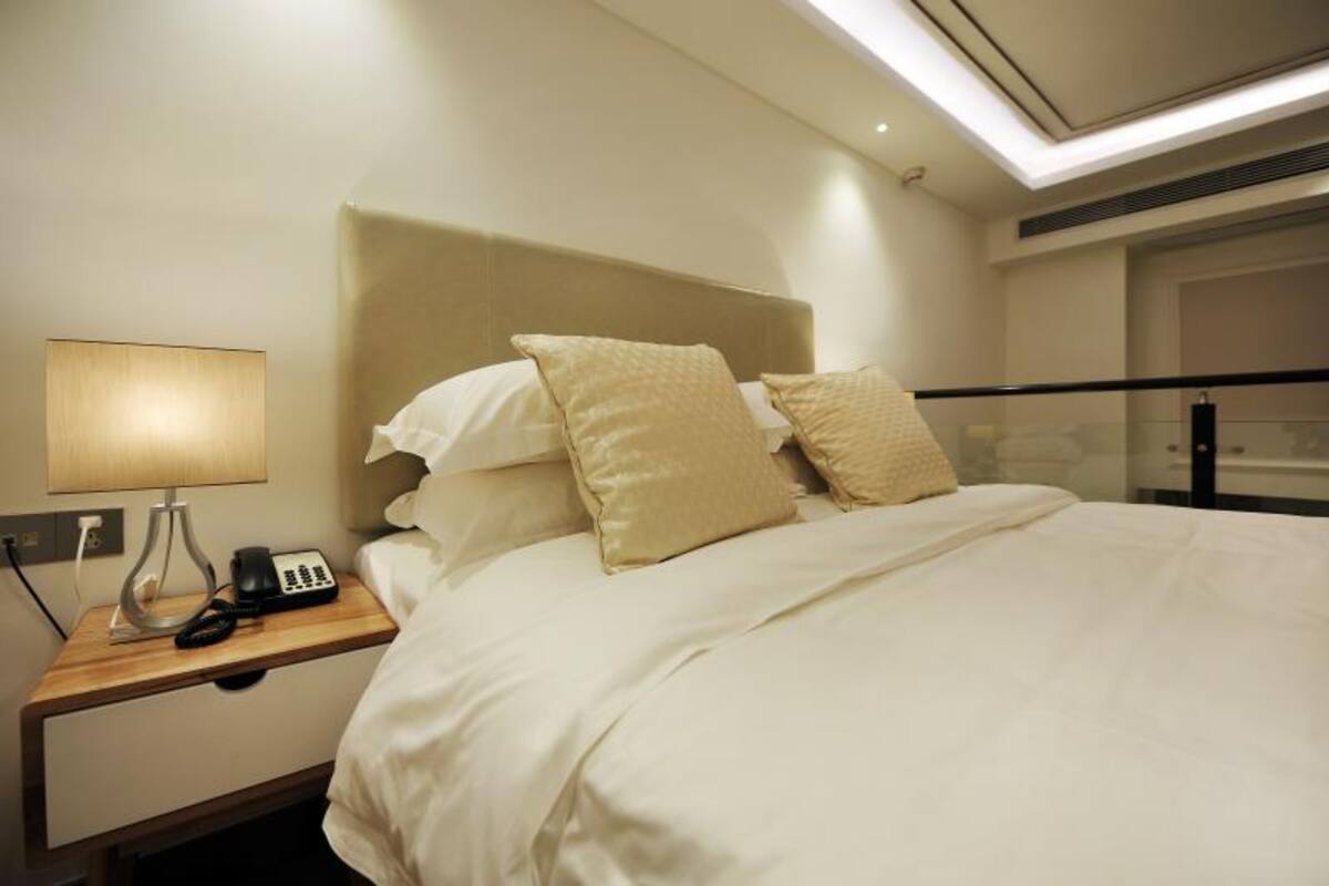 A hotel room with a bed, a bedside lamp, a phone, and a glass partition.