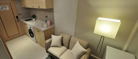 A compact kitchenette with a washing machine, a sofa, and a floor lamp.
